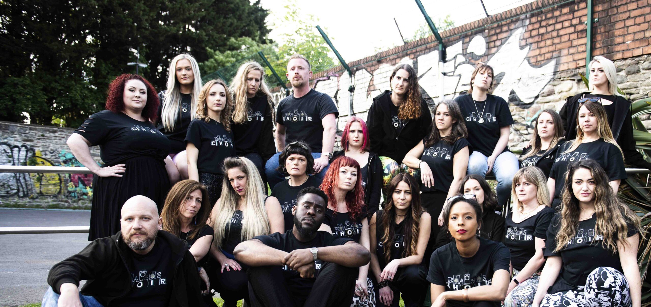 A diverse group of individuals smiling and posing together for a group photo in a bright outdoor setting.