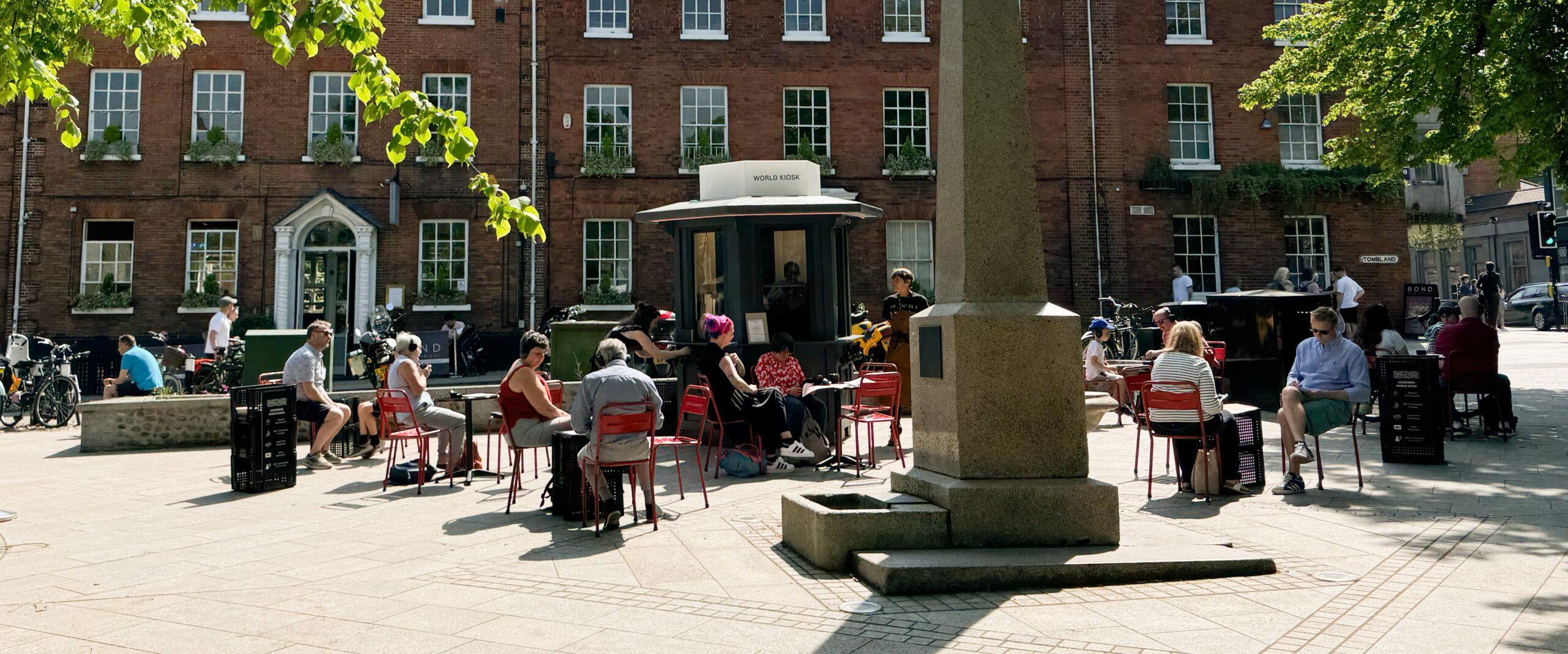 Community members gathered outside the World Kiosk on a bright day.