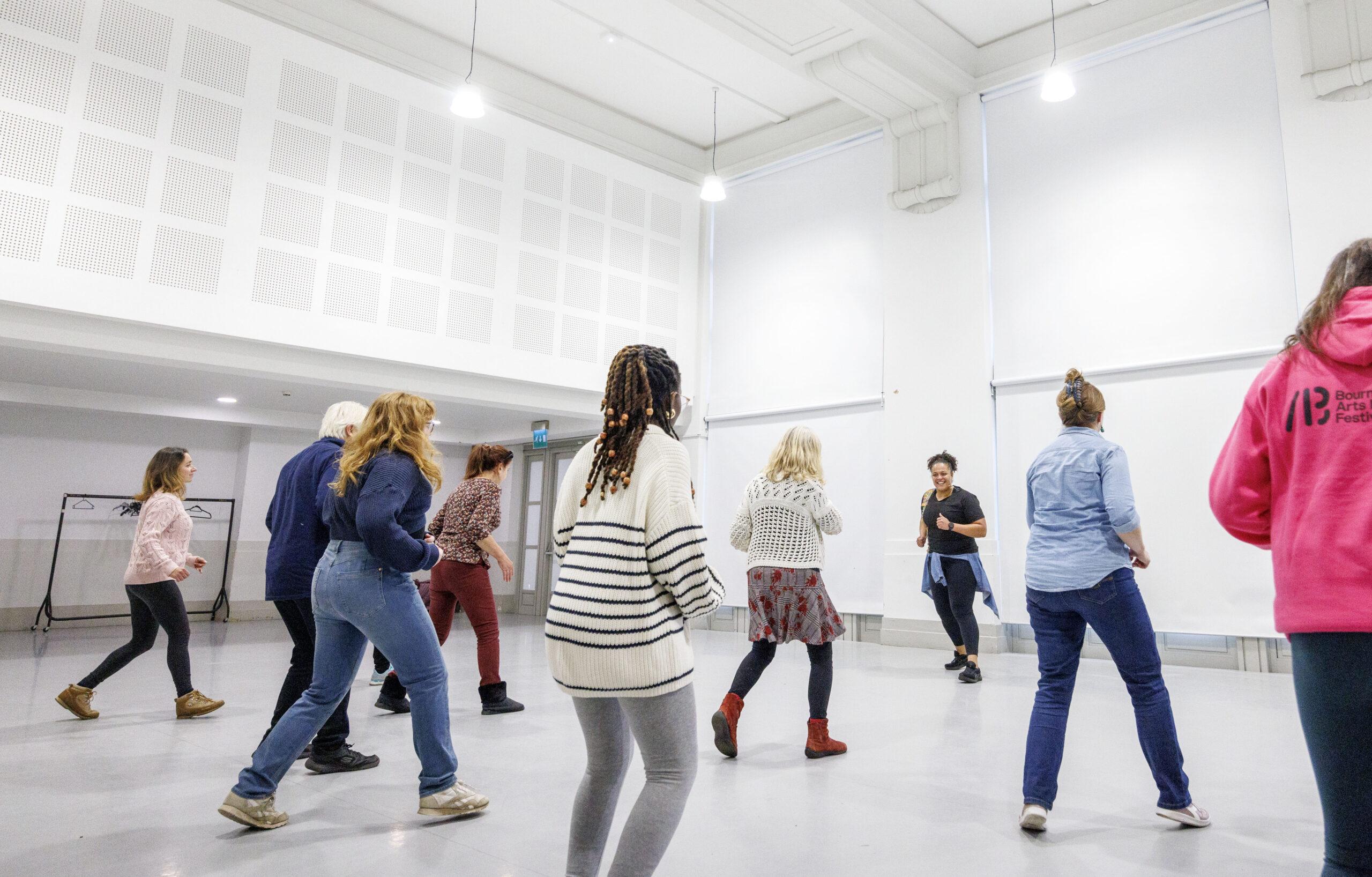 People join a dance workshop in a bright room, following an instructor’s lead, with a Bournemouth Arts Festival hoodie visible.